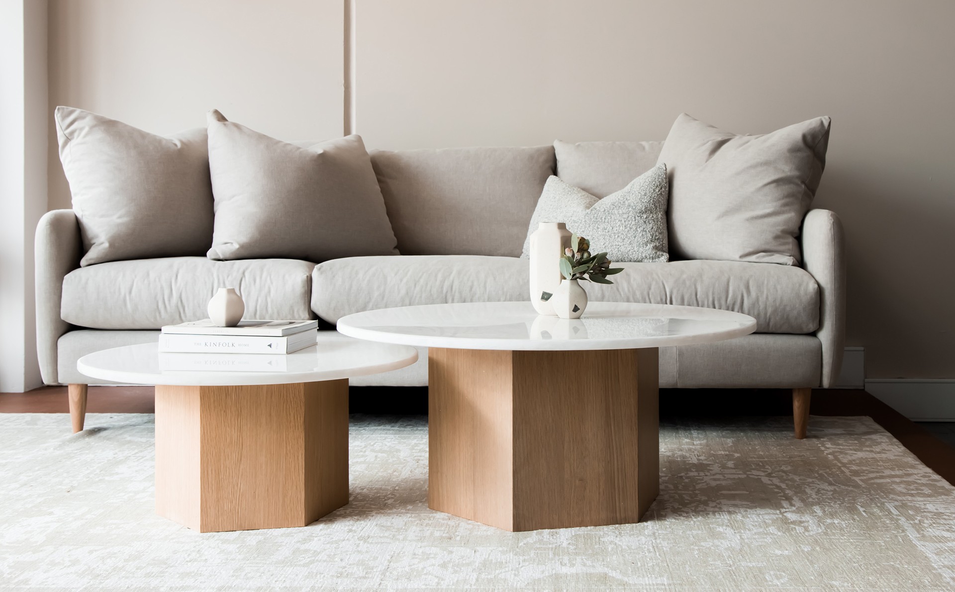 Dwa okrągłe marmurowe stoliki z drewnianą podstawą stoją na jasnym dywanie na tle jasnobeżowej sofy z drewnianymi nóżkami Home Staging oferta