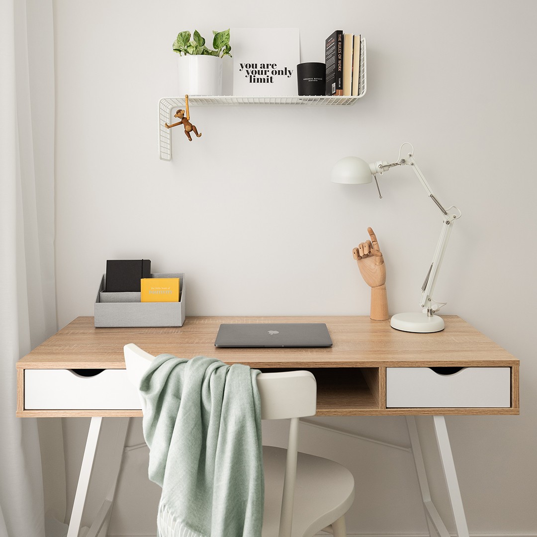 Drewniane biurko po stylizacji wnętrz. Nad biurkiem metalowa półka z kwiatkiem w białej doniczce, motywacyjną grafiką, świecą, książkami i małpką Kaya Bojesena.