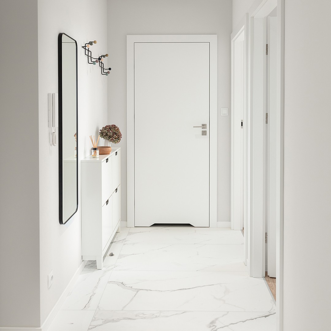 Biały korytarz z marmurowymi płytkami na podłodze i białą szafką na buty po home stagingu warszawa