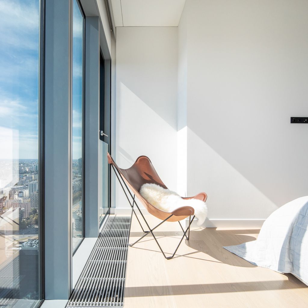 Nowoczesny skórzany fotel z białą owczą skórą, stojący w przeszklonej sypialni z pięknym widokiem na Warszawę. 36 piętro w budynku Cosmopolitan