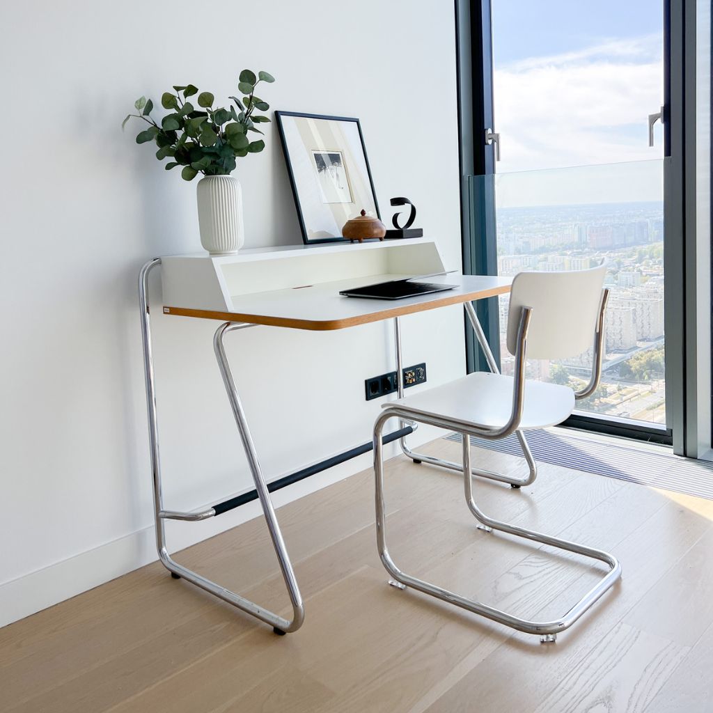 Gabinet z widokiem na warszawskie wieżowce po home staging. Białe nowoczesne biurko i krzesło na metalowych nogach. Na biurku laptop, wazon z kwiatami i dekoracje